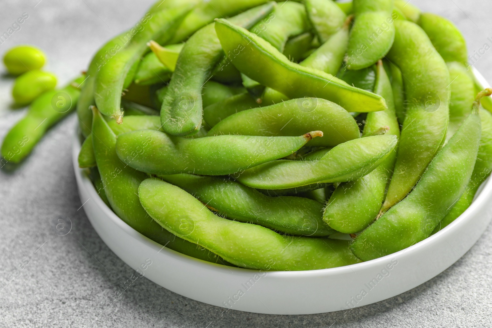 Photo of Plate with green edamame beans in pods on light grey table, closeup