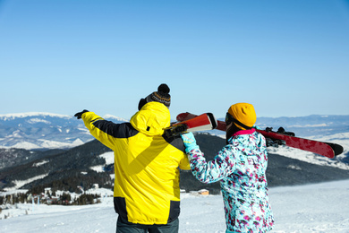 Photo of Couple with ski equipment in mountains, back view. Winter vacation