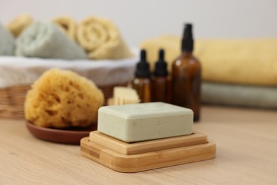 Photo of Soap bar, sponge and bottles of essential oils on light wooden table. Spa therapy