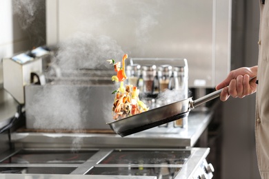 Male chef cooking tasty food on stove in restaurant 
kitchen, closeup of hand