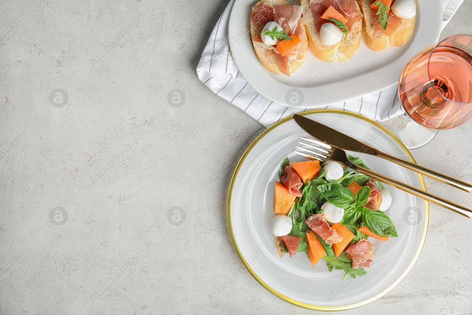 Photo of Flat lay composition of fresh melon with prosciutto on light grey table. Space for text