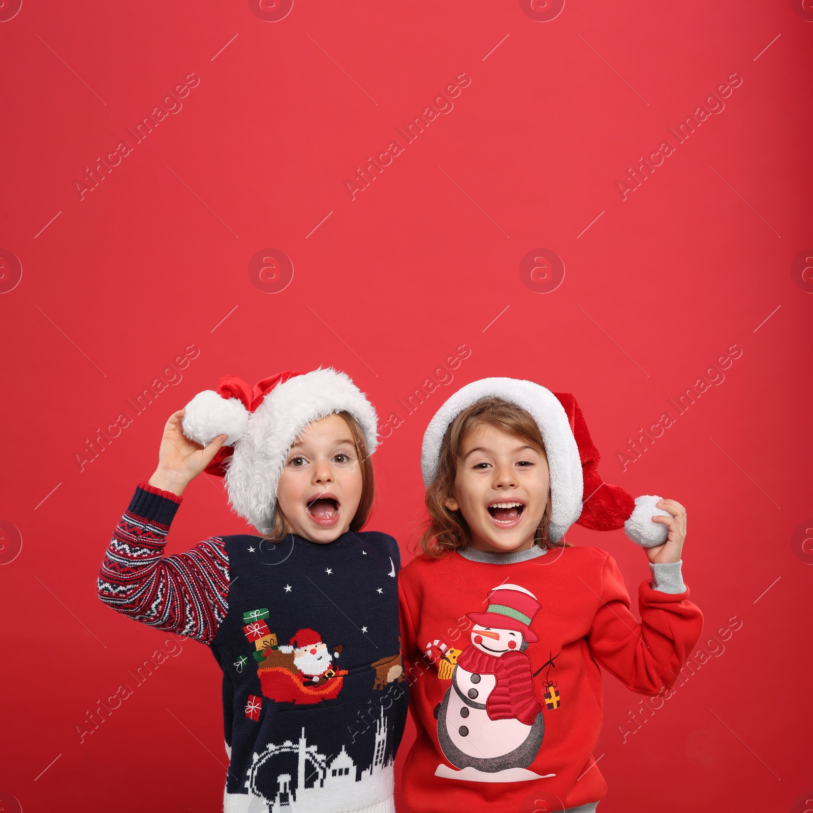 Photo of Kids in Christmas sweaters and Santa hats on red background