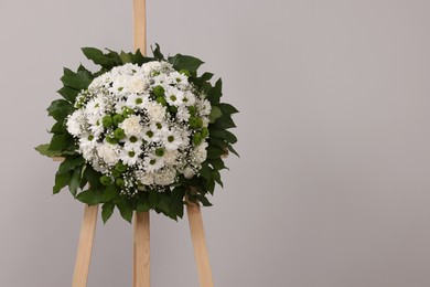 Funeral wreath of flowers on wooden stand against grey background. Space for text
