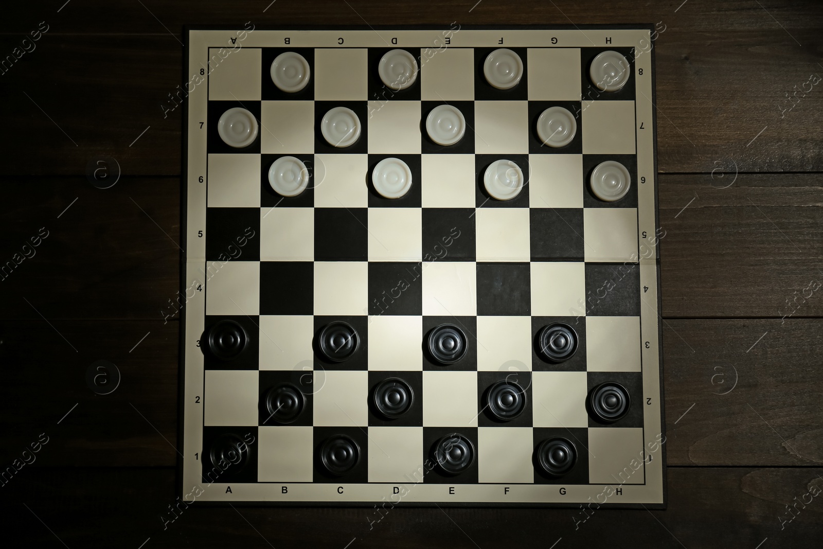 Photo of Checkerboard with game pieces on wooden table, top view