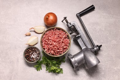 Photo of Manual meat grinder with beef mince, peppercorns, onion and parsley on light grey table, flat lay
