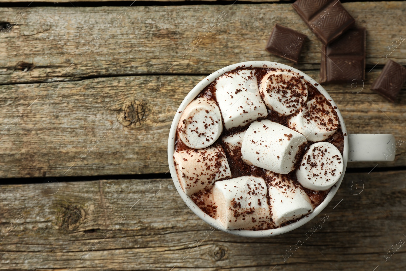 Photo of Delicious hot chocolate with marshmallows, cocoa powder and pieces on wooden table, top view. Space for text
