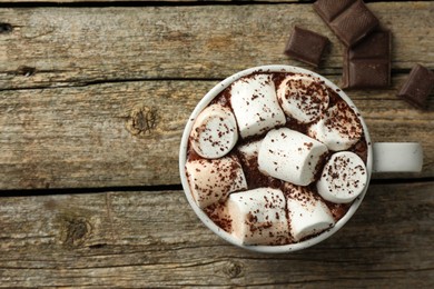 Delicious hot chocolate with marshmallows, cocoa powder and pieces on wooden table, top view. Space for text