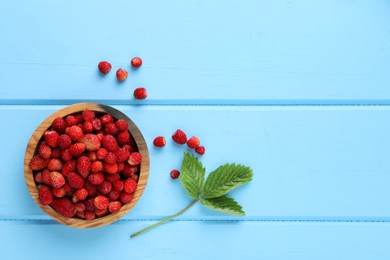 Photo of Fresh wild strawberries in bowl near leaves on light blue wooden table, flat lay. Space for text