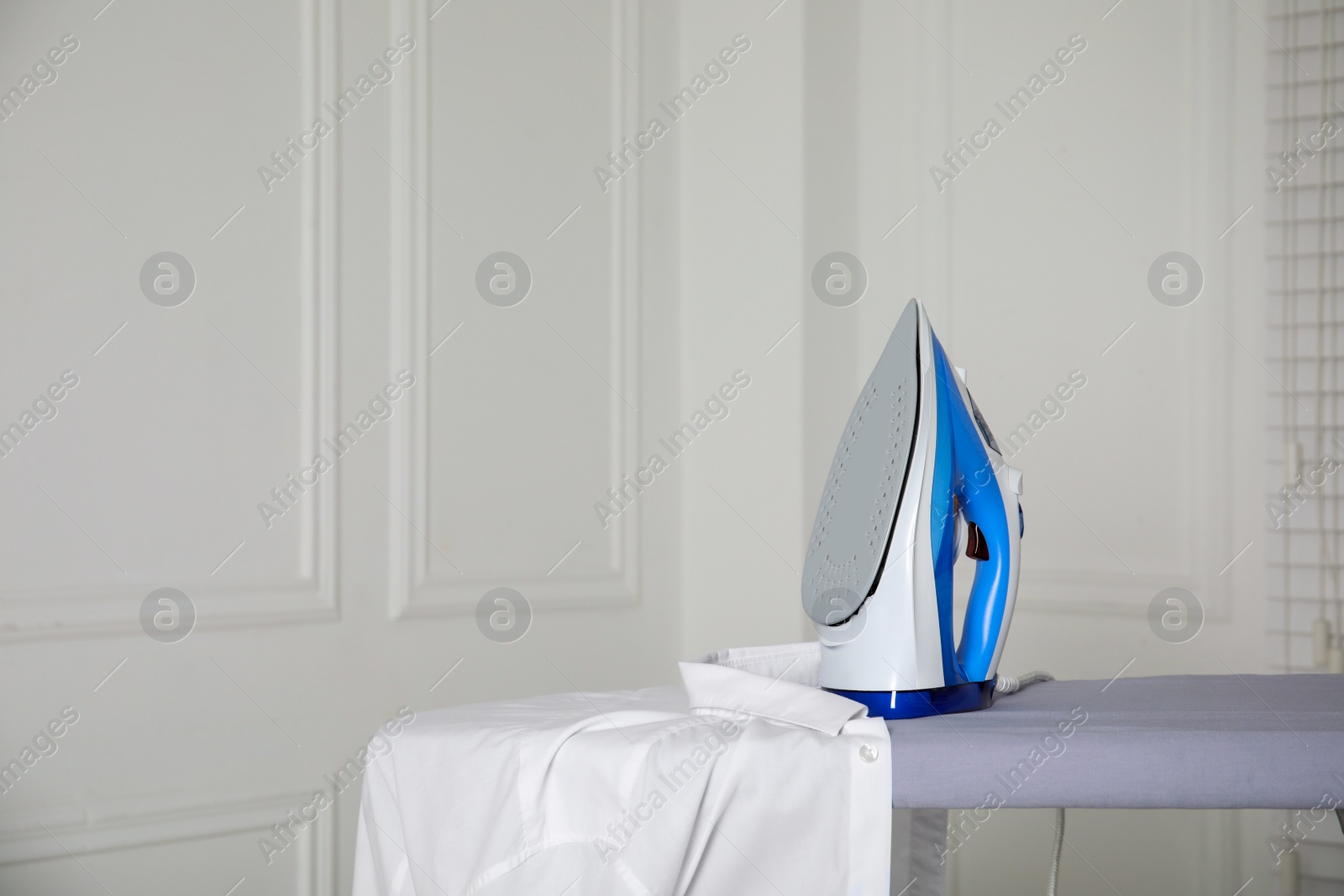 Photo of Modern iron and clean shirt on board indoors, space for text