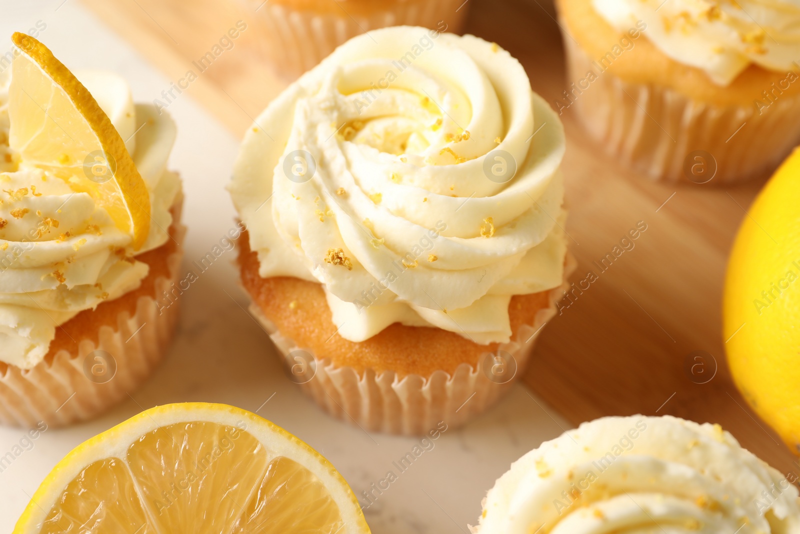 Photo of Tasty cupcakes with cream and lemon zest on board, closeup