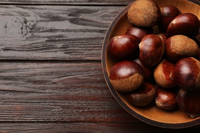 Photo of Sweet fresh edible chestnuts in bowl on wooden table, top view. Space for text