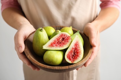 Woman holding bowl with fresh ripe figs on light background