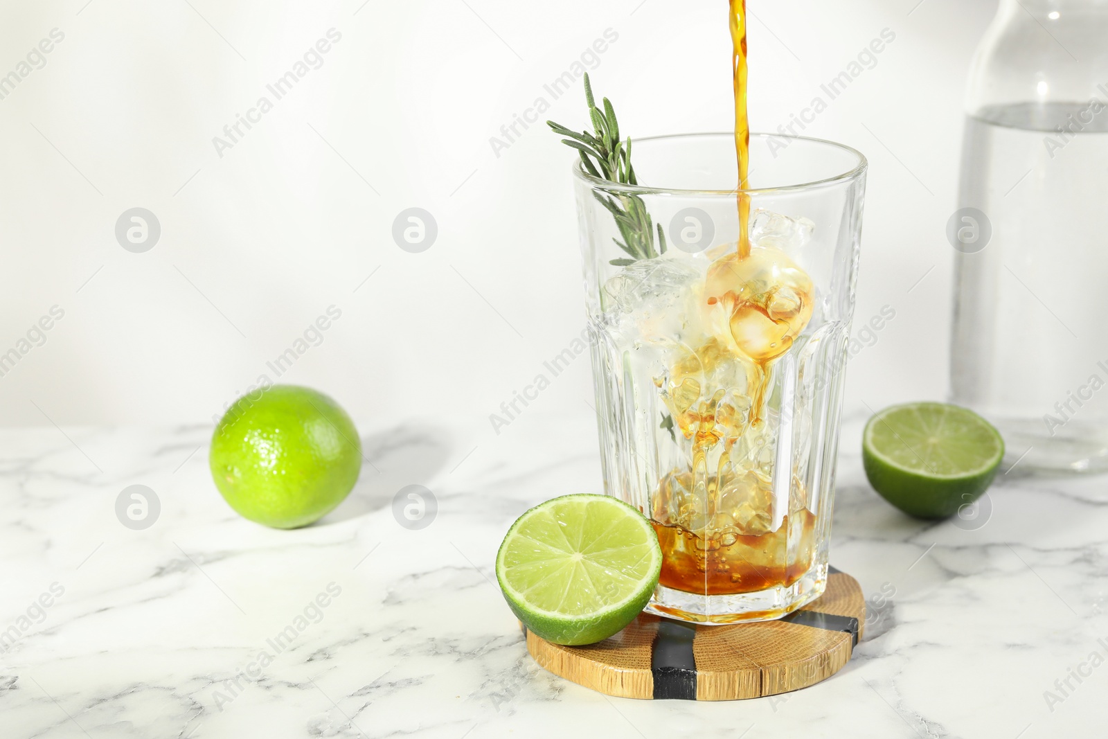 Photo of Pouring coffee into glass with ice cubes at white marble table. Space for text