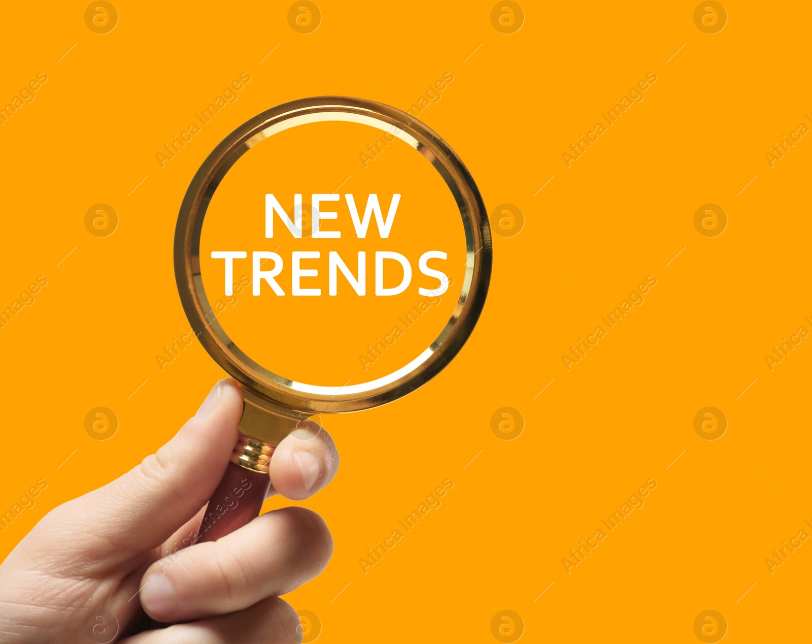 Image of Searching new and popular trends. Woman holding magnifying glass over words on orange background, closeup