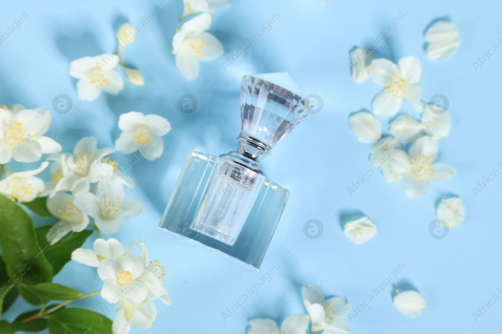 Photo of Aromatic perfume in bottle and beautiful jasmine flowers on light blue background, flat lay