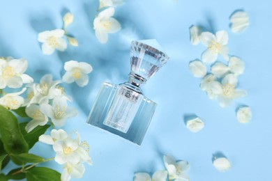 Aromatic perfume in bottle and beautiful jasmine flowers on light blue background, flat lay