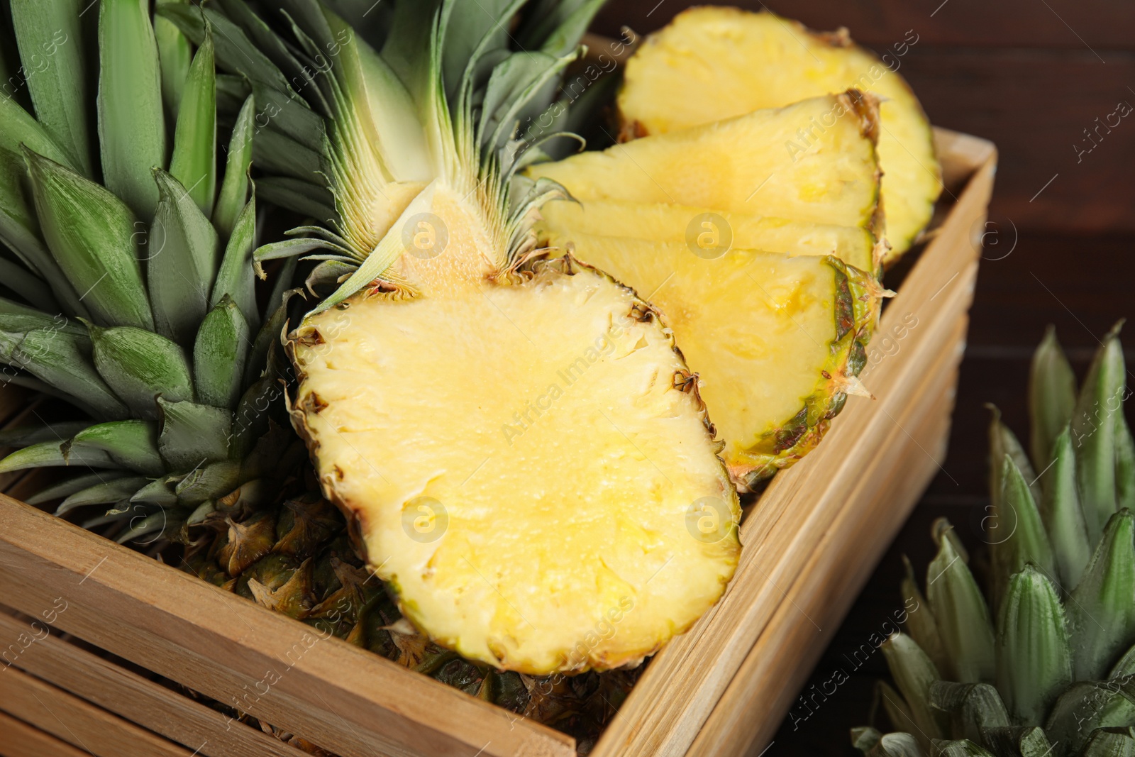 Photo of Tasty cut pineapples in wooden crate on table, closeup