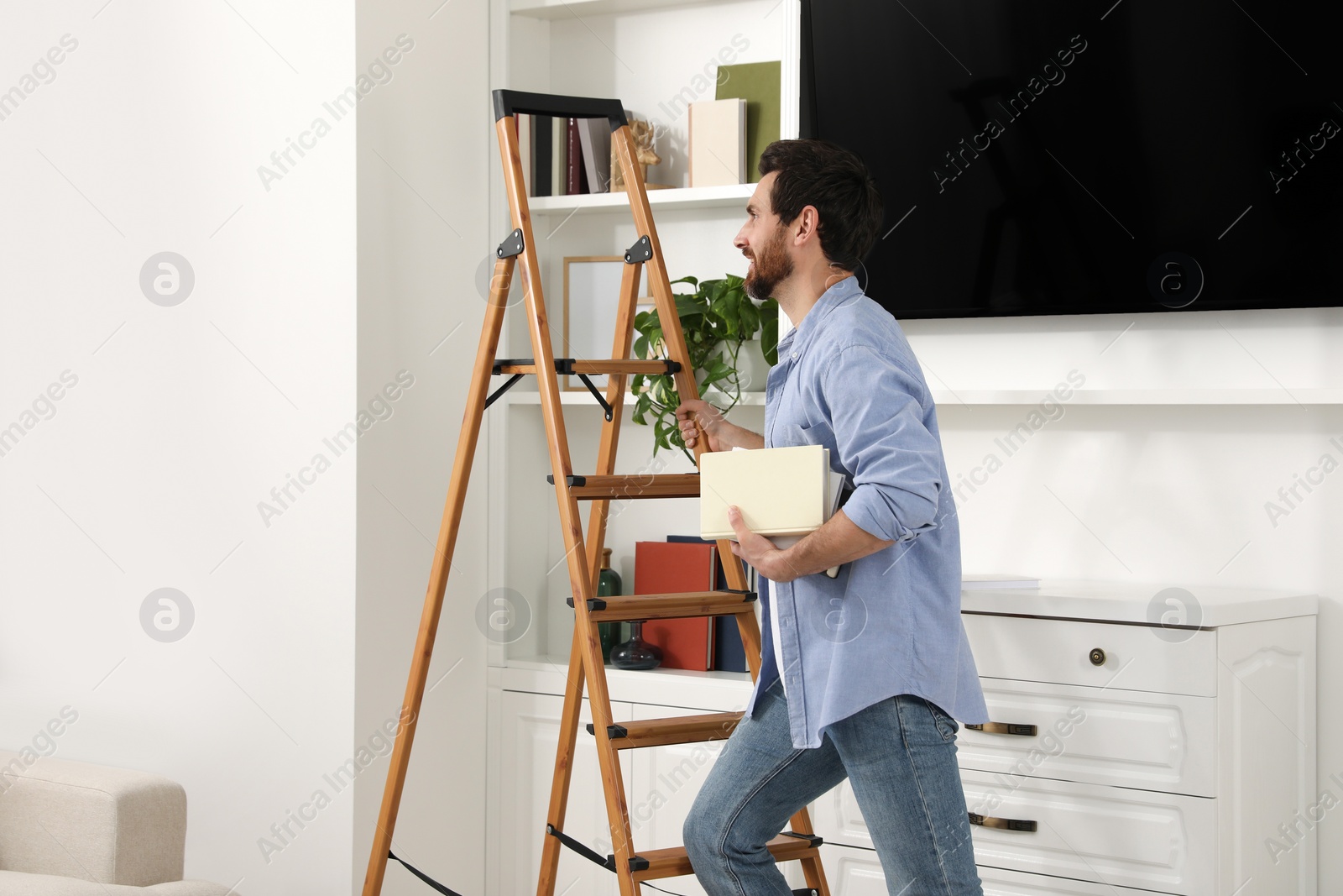 Photo of Man with books on wooden folding ladder at home