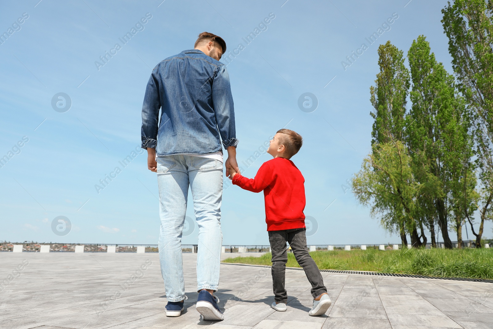 Photo of Little child holding hands with his father outdoors. Family weekend