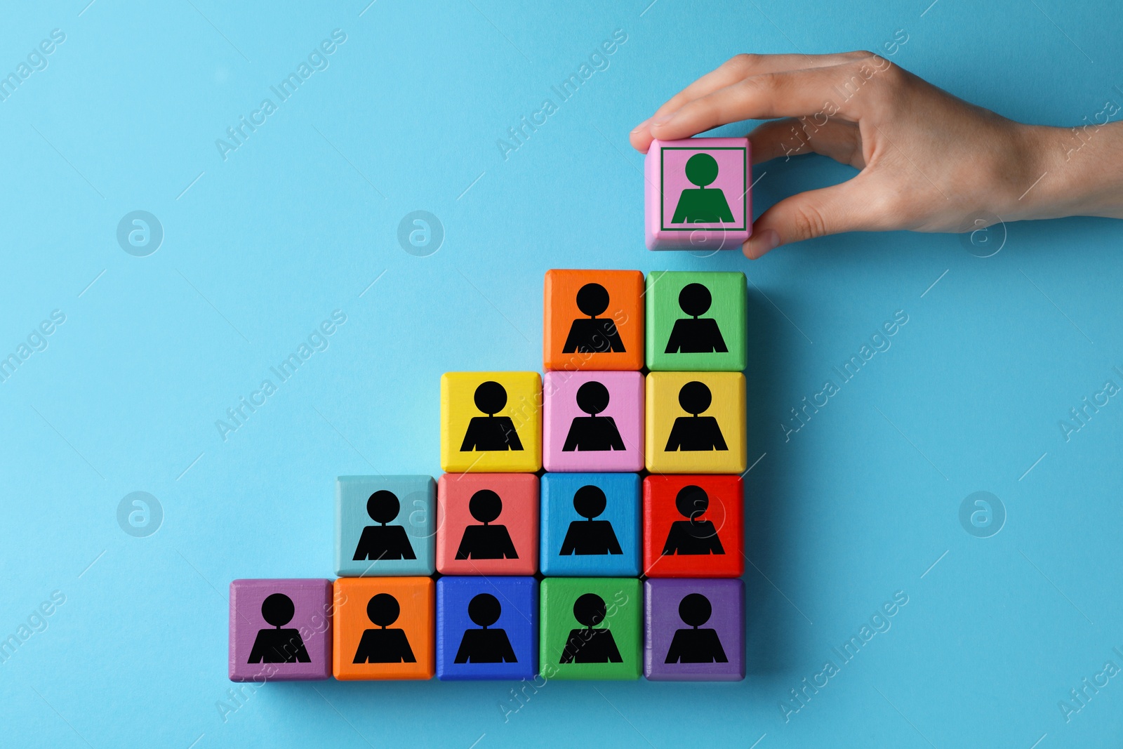 Image of Woman putting cube with green human icon on top of others with black ones on light blue background, closeup