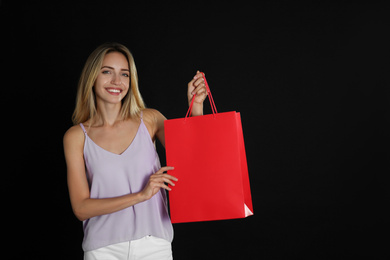 Photo of Happy young woman with shopping bag on dark background. Black Friday Sale