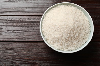 Photo of Raw basmati rice in bowl on wooden table, top view. Space for text