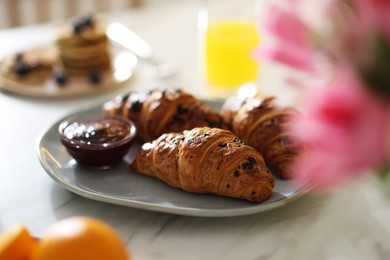 Photo of Tasty breakfast. Plate with fresh croissants and jam on white marble table, closeup