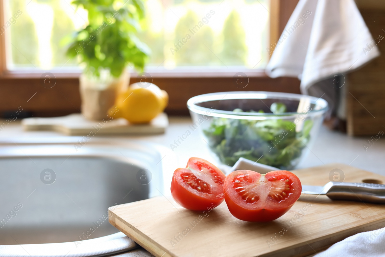 Photo of Cut fresh tomato and knife near sink in kitchen, space for text