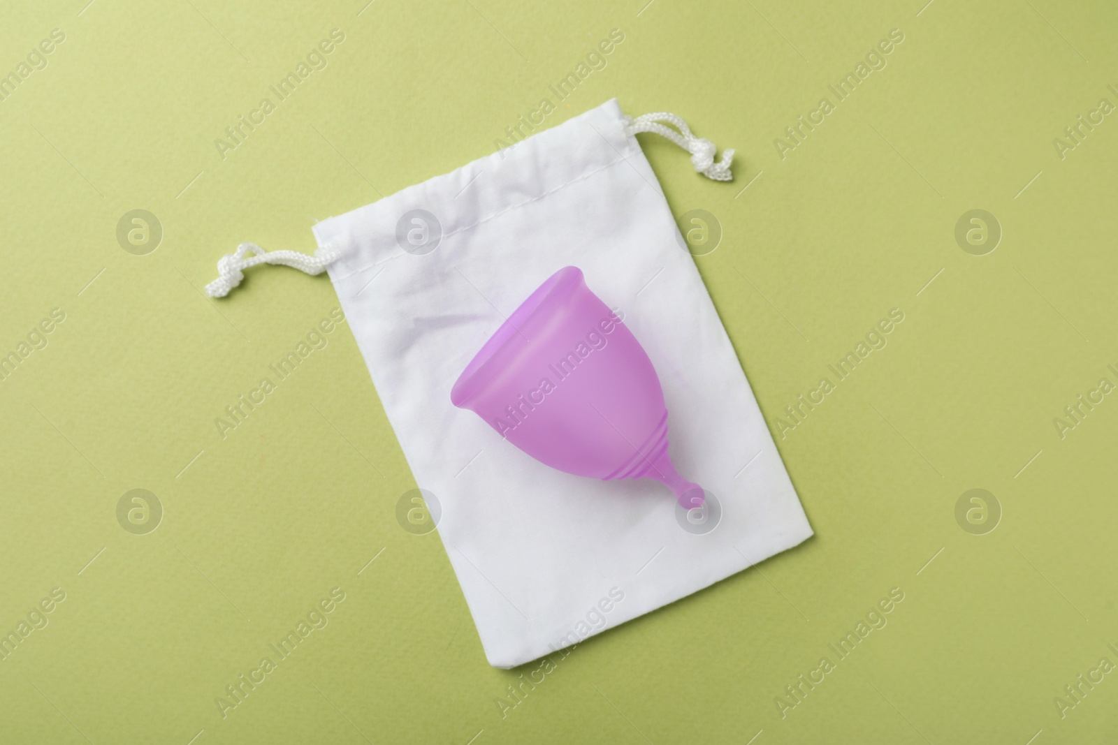 Photo of Menstrual cup with cotton bag on green background, top view