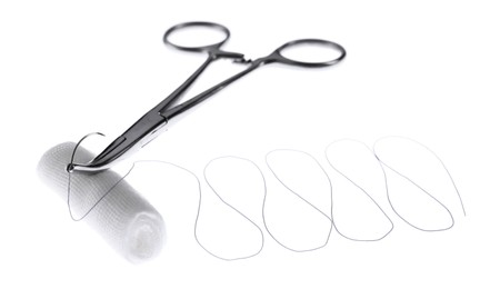 Photo of Forceps with suture thread and bandage roll on white background. Medical equipment