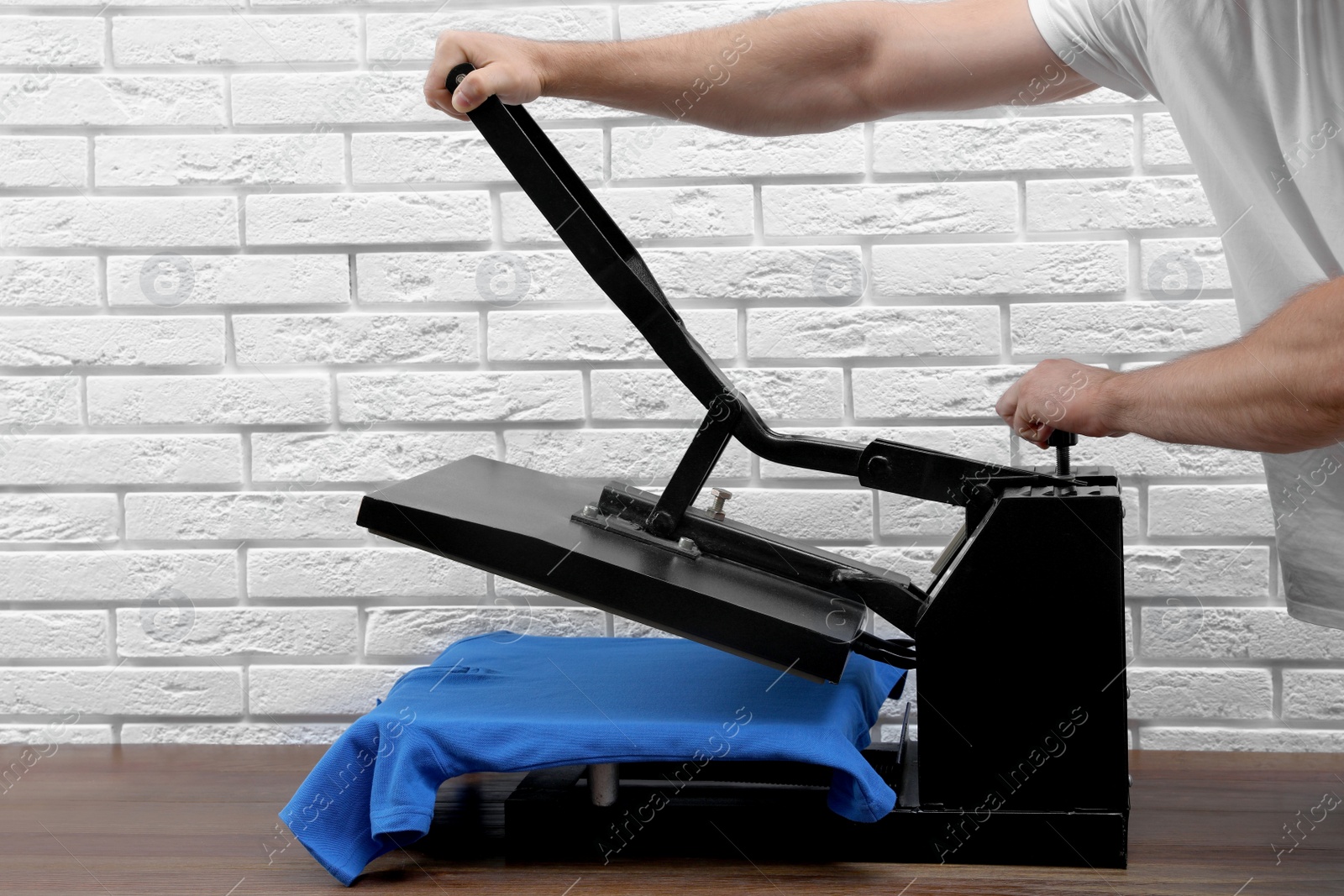 Photo of Man using heat press machine at table near white brick wall, closeup