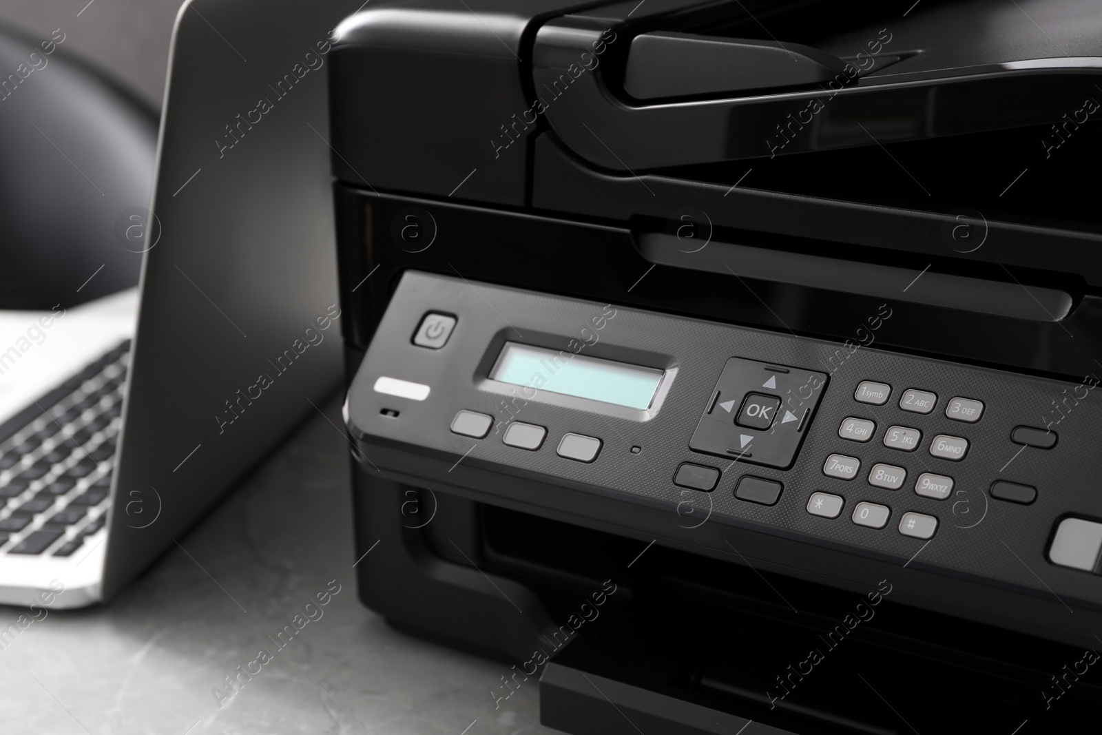 Photo of New modern printer and laptop on grey table, closeup