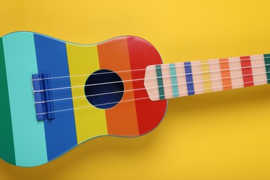 Colorful ukulele on yellow background, top view. String musical instrument