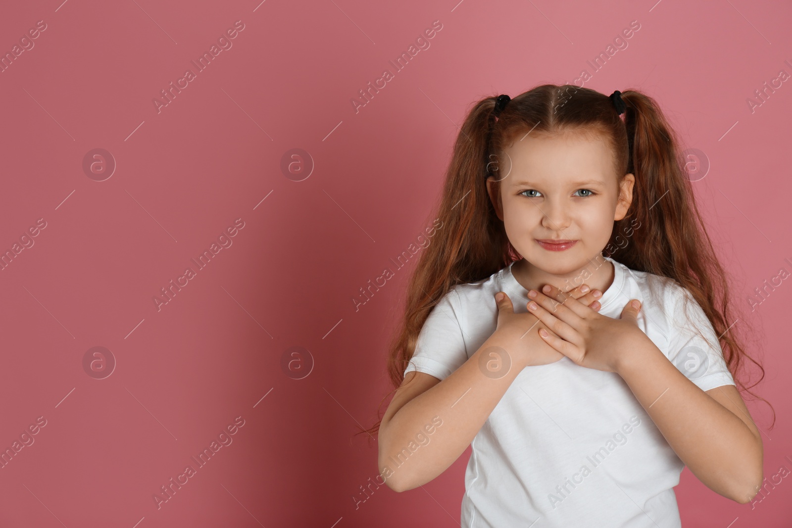 Photo of Cute grateful little girl with hands on chest against pink background. Space for text