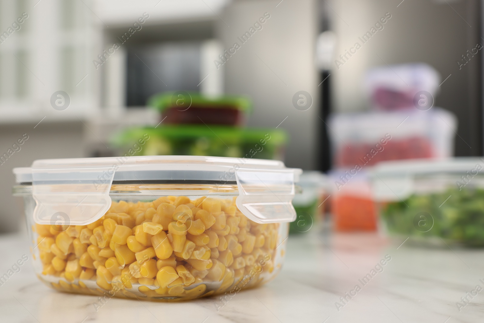 Photo of Glass container with tasty corn kernels on white marble table in kitchen, closeup and space for text. Food storage