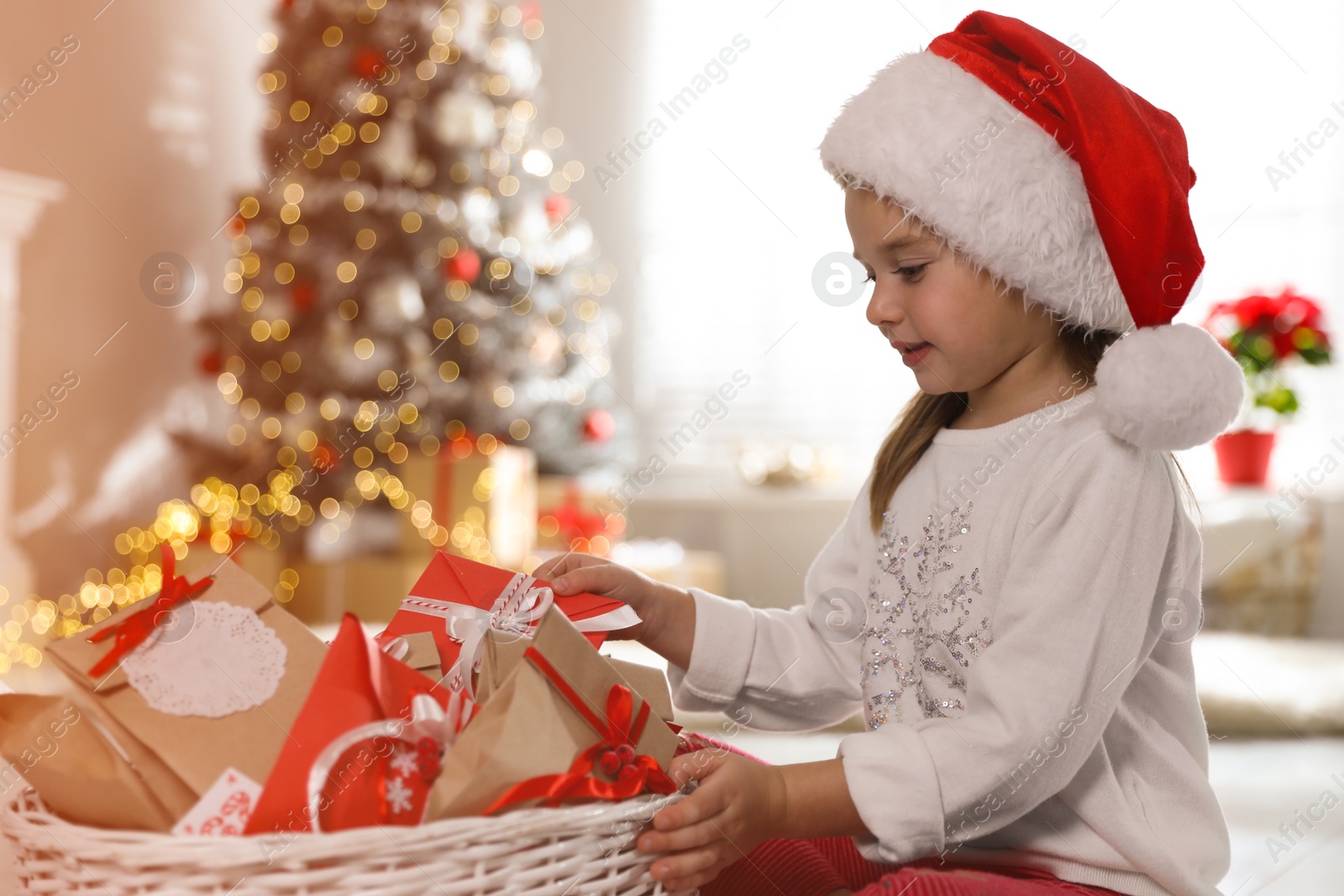 Photo of Cute little girl in Santa hat taking gift from Christmas advent calendar at home