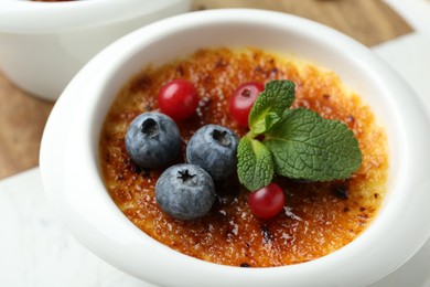 Delicious creme brulee with berries and mint in bowl on table, closeup