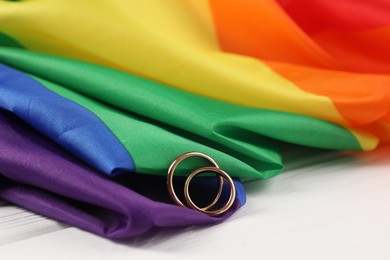 Rainbow LGBT flag and wedding rings on white wooden table, closeup