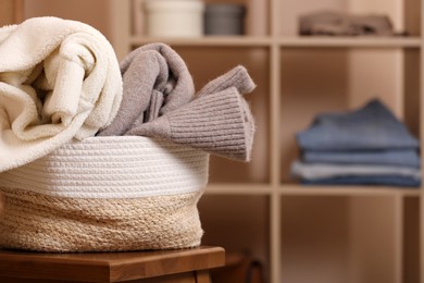 Photo of Wicker laundry basket overfilled with clothes on wooden stool indoors, closeup. Space for text