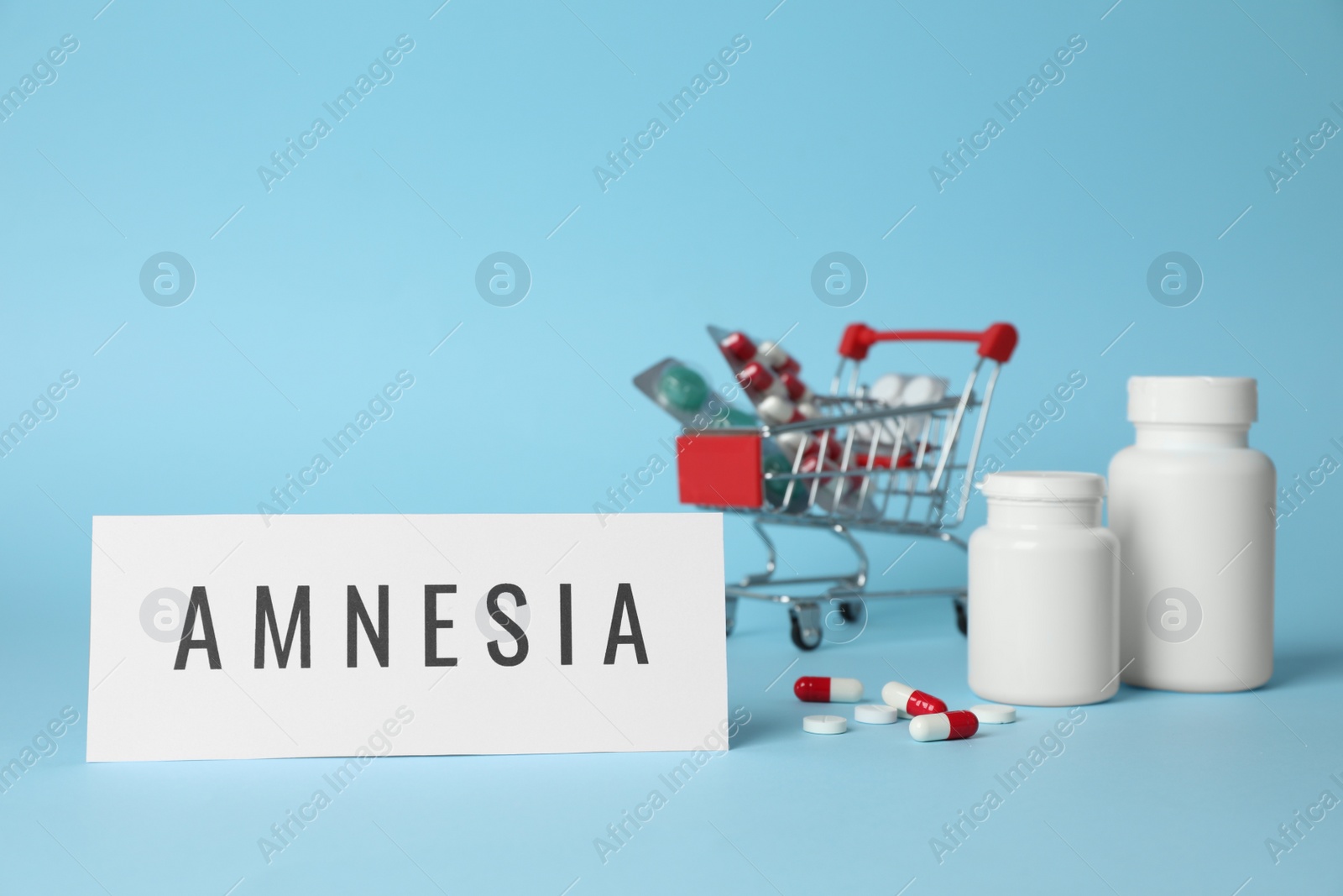 Photo of Card with word Amnesia and pills on light blue background