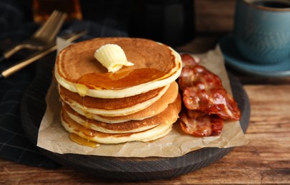 Photo of Delicious pancakes with maple syrup, butter and fried bacon on wooden table