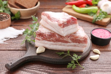 Photo of Pieces of tasty pork fatback with garlic and parsley on wooden table