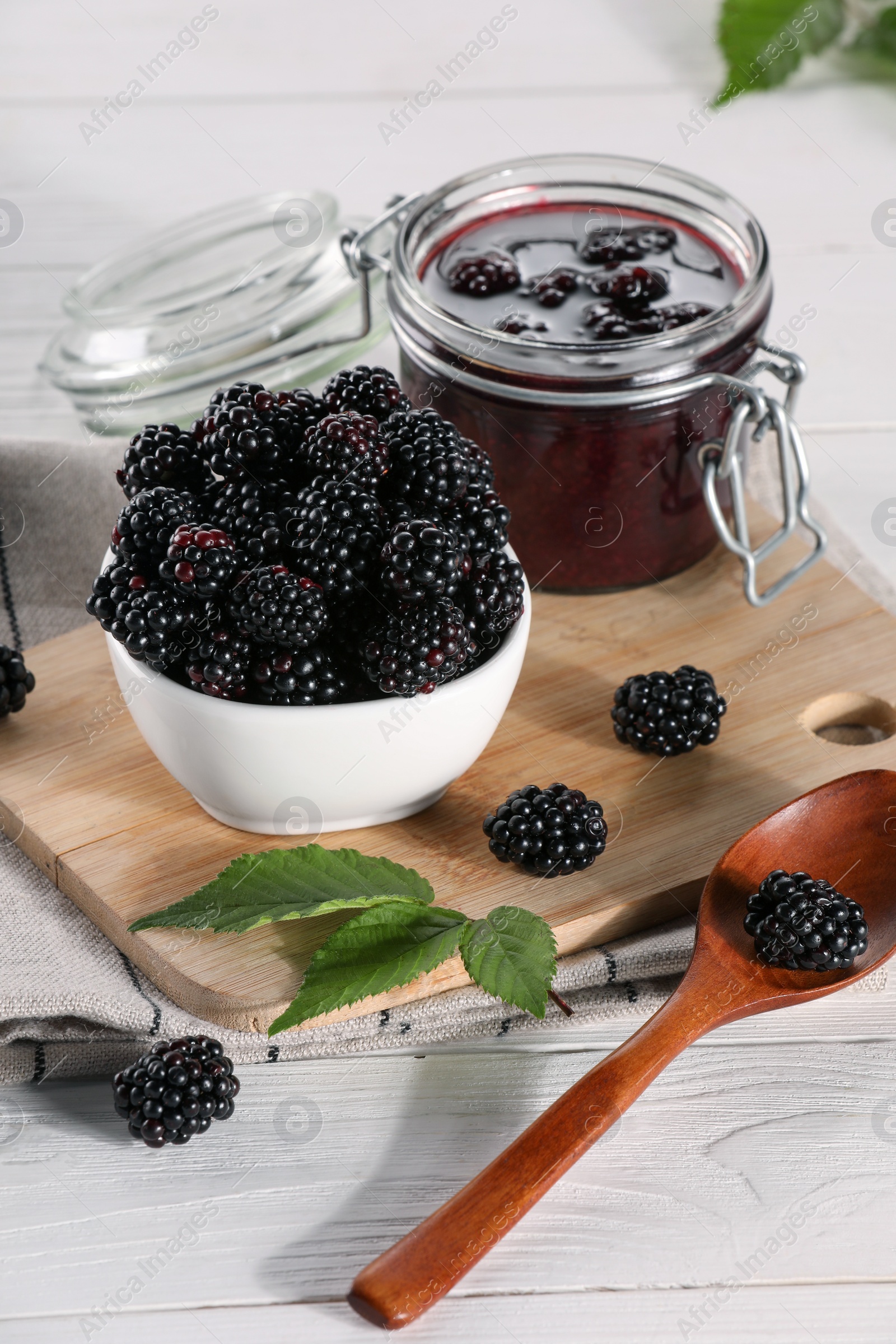 Photo of Fresh ripe blackberries, tasty jam and leaves on white wooden table