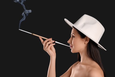 Photo of Woman using long cigarette holder for smoking on black background