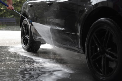 Photo of Man washing auto with high pressure water jet at outdoor car wash, closeup