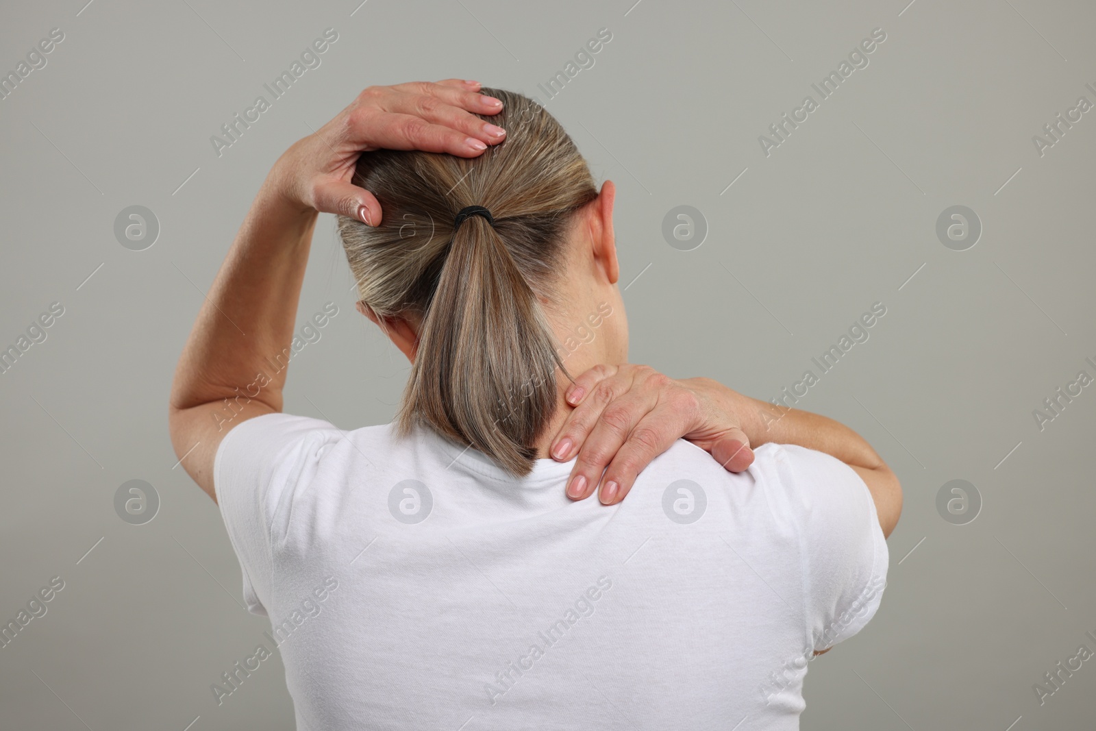 Photo of Mature woman suffering from pain in her neck on grey background, back view