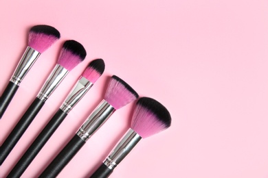 Flat lay composition with set of professional makeup brushes on pink background. Space for text