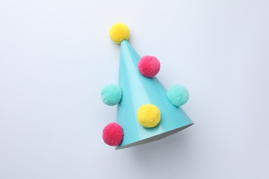 Photo of One blue party hat with pompoms on light background, top view