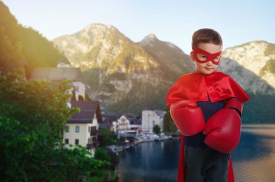 Superhero, motivation and power. Boy in cape and mask wearing boxing gloves in mountains
