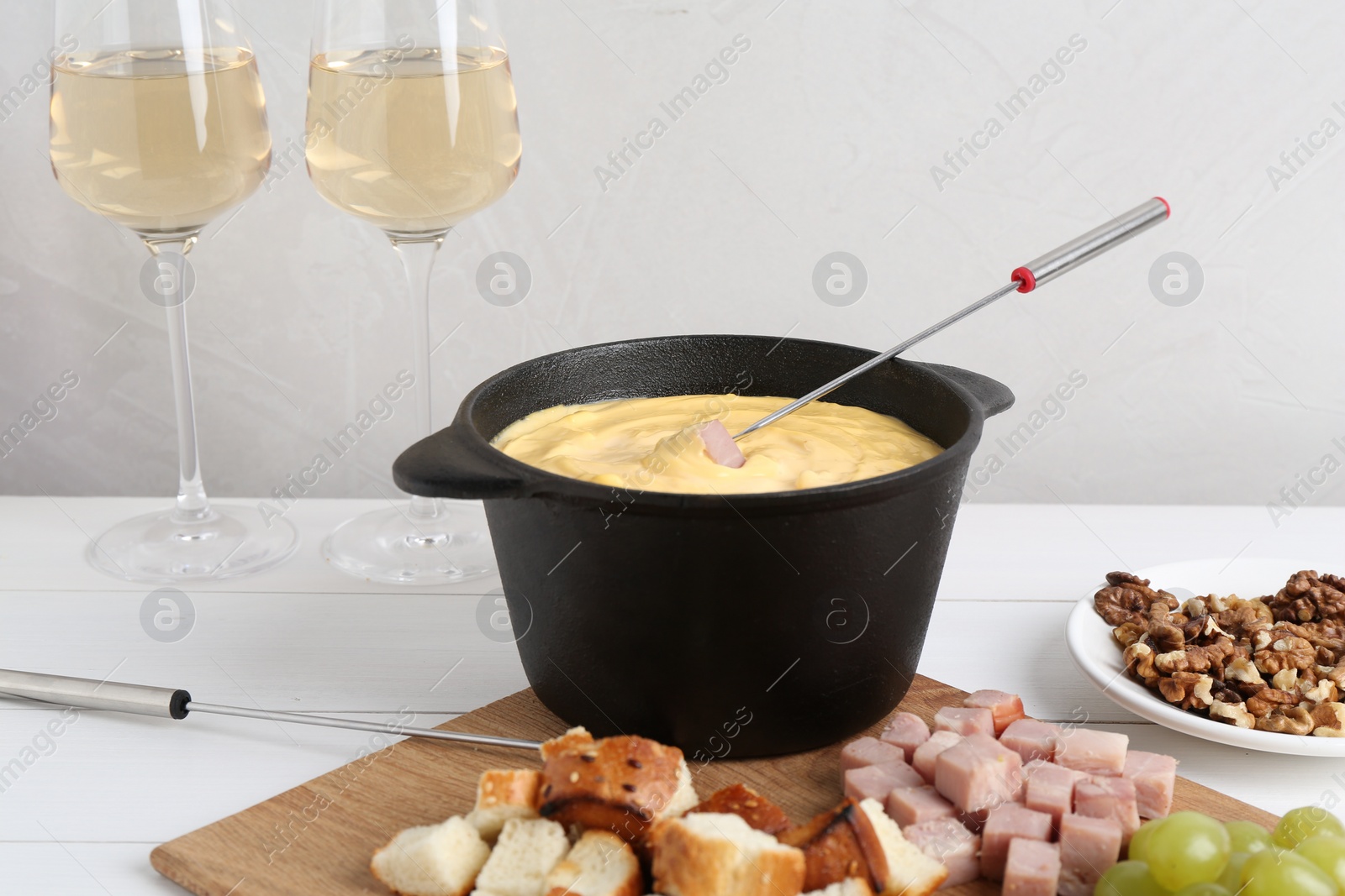 Photo of Fondue pot with tasty melted cheese, forks, wine and different snacks on white wooden table